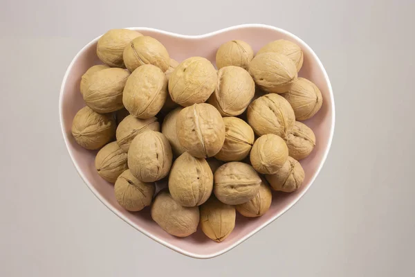 Inshell walnuts in a heart-shaped plate. Heart Nuts, Heart Health Products, Structured Walnuts — Stock Photo, Image