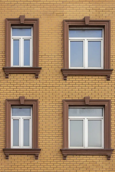 4 plastic windows in the brick house of yellow bricks. Beautiful windows with moldings and brown trim. Modern design of windows