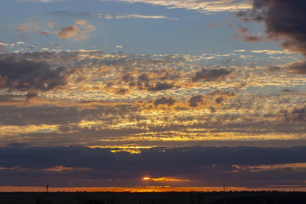 Beautiful sunset. The sun sets over the horizon turns dark clouds in orange yellow.