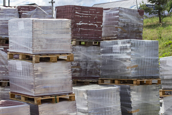 Building materials on pallets, red bricks paving stone. Warehouse building materials in the open. Bricks and building blocks