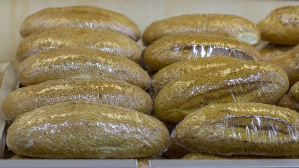 Loafs of fresh grain bread wrapped in polyethylene on a pallet with fresh bread — Stock Photo, Image