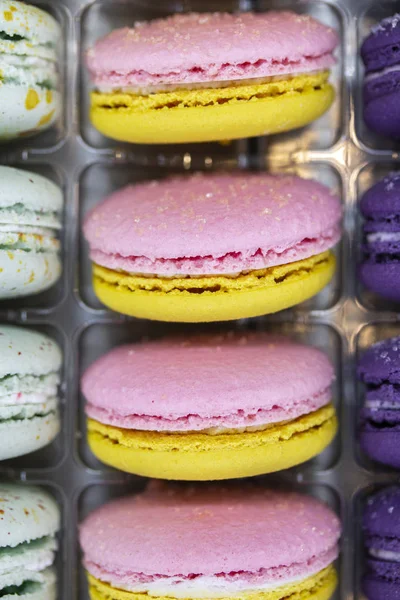 French macaroons dessert range lilac yellow with plastic case. Sweet macaroons cookies for tea. Two-colored macaroon with cream in the middle. — Stock Photo, Image