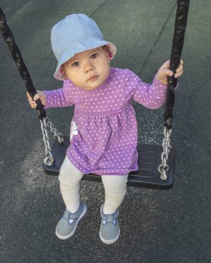 Mor elbiseli küçük kız bir salıncak, koyu bir arka plan, bir çocuk portresi sürme. Sevimli ciddi genç kız bir salıncak, yumuşak odak üzerinde oturan