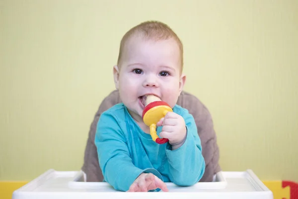 Kaukasische peuter baby 5 6 maanden jongen meisje zit op een hoge stoel en eet fruit van een Nibbler. Kid kind leert te eten, portret zachte focus — Stockfoto