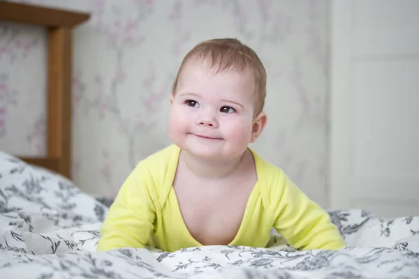 Kleine Europese 7 maanden baby meisje jongen in geel. Schattig kind werpt zijn lichaam in zijn armen, glimlacht slyly, je zijn ogen — Stockfoto