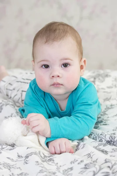 Baby 6 hónap egy kék pulóver és csíkos rövidnadrág feküdt az ágyon. Chubby arcát kisgyermek portré Közelkép. Lány fiú európai függőleges portré — Stock Fotó