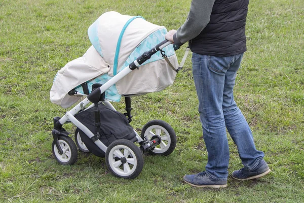 Father walks with carriage, bottom view only legs. Bright mint stroller and legs in jeans, walking with a child outdoor Royalty Free Stock Images