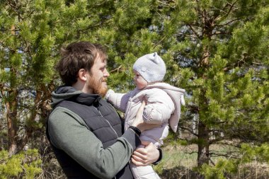 Kollarında bebek olan bir baba parkta yürüyor. Sakallı genç bir adam 9 ay çocuk kız tutar