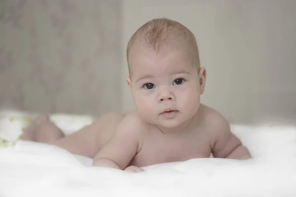 Aranyos újszülött fiú lány fekszik az ágyon, és óvatosan néz a kamerába. Európai Baby kölyök, Soft Focus — Stock Fotó