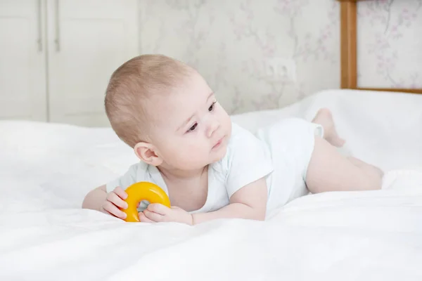 Bebê de branco no quarto. Uma criança pequena segura um brinquedo . — Fotografia de Stock