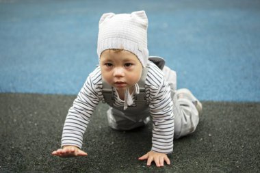 Gri elbiseli oğlan çocuk parkında sürünüyor. Çocuk dört ayak üstünde