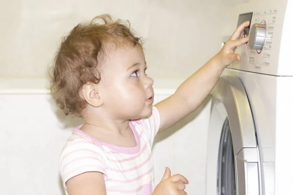 Het kleine meisje drukt op de knoppen van de wasmachine. Europees blank kind en wasmachine — Stockfoto