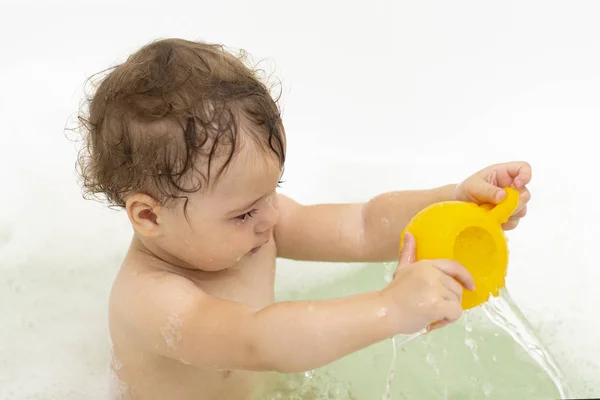 Egy kisgyerek fürdik a kádban, a kisfiú a vízben ül szappanhabban. — Stock Fotó