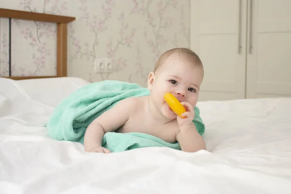 Baby blank meisje jongen verpakt in een handdoek, knabbels op een plastic bagel, zachte focus — Stockfoto