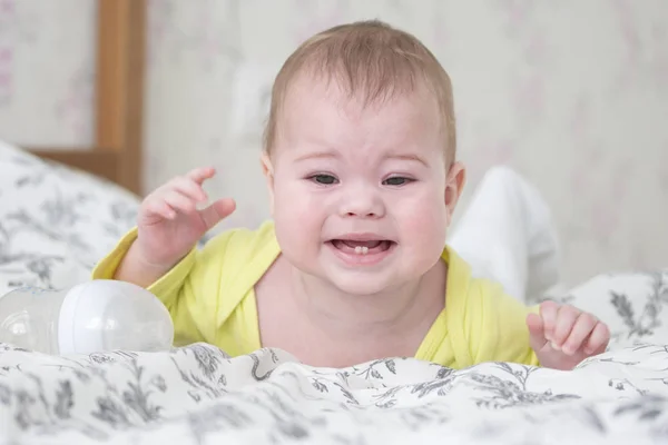 Baby 6-7 maanden huilen liggend op zijn buik. Een blanke baby in het geel huilt en toont 2 baby tanden, tandjes, portret zachte focus — Stockfoto