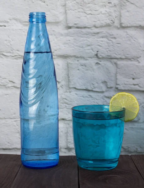 A blue glass and a bottle of water agua pure with a circle of lemon A concept of pure water that brings life and health — Stock Photo, Image