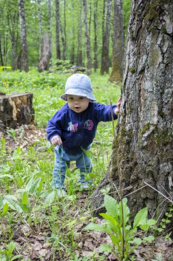 Şapkalı ve kot pantolonlu bebek suratı şaşırdı. Bebek 9 ay boyunca orman çimlerini ve ağaçlarını keşfetti. Doğadaki ilk adımlar