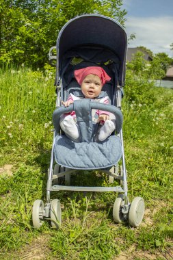 Pembe fularlı neşeli şirin kız mavi bebek arabasıyla yürüyor. Bebek kız 9 ay bacak muhabbeti yaz arabasında oturan küçük gülümseyen çocuk, yaz günü