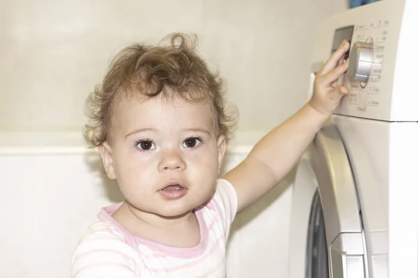 Pouco caucasiano menina hooligan aperta o botão de uma máquina de lavar roupa — Fotografia de Stock
