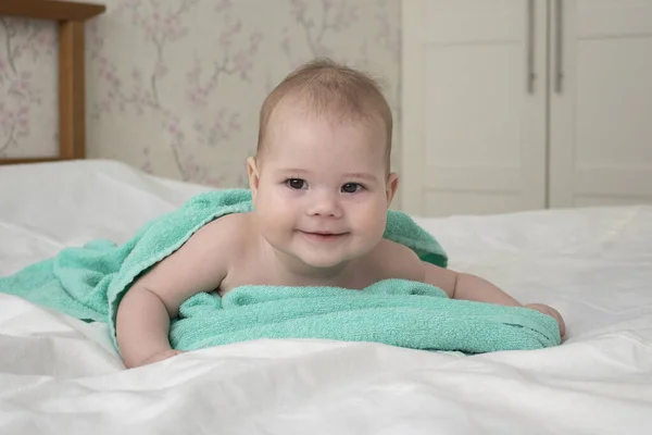 Lachend baby kind ligt gewikkeld in een handdoek na het baden. vrolijke positieve meisje jongen ondeugende blik. Baby portret zachte focus — Stockfoto