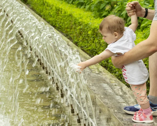 Детские розовые сандалии играют с водой. Ребенок касается воды в фонтане, засовывает руки под струи воды. Девушка в фонтане — стоковое фото
