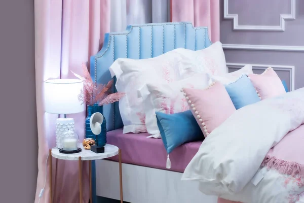 Pastel mavisi, güzel bir yatak odasının arka planının altını oyuyor. Büyük bir yatak, bir sürü yastık, içinde lamba vazosu ve süslemeleri olan bir komodin.