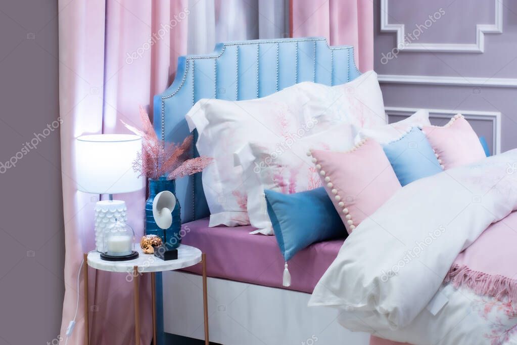 Defocus background of a beautiful bedroom in pastel pink blue. A large bed, a bunch of pillows, a bedside table with a lamp vase and decorations