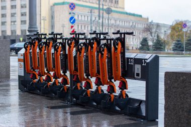 12-10-2019, Moskova, Rusya. 12-10-2019, Moskova, Rusya. Ulaşım ve spor aletleri için şehir kirası, kiralık scooterlı otomatik bir raf. Turuncu mobiletler katlı, yağmurlu havada asılı