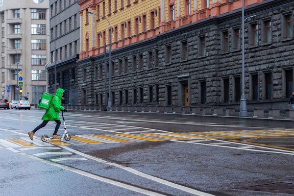 12-10-2019, Moscow, Russia. 12-10-2019, Moscow, Russia. Delivery Club courier rides a scooter through a pedestrian crossing with a large backpack with food. Food delivery at home in any weather, rain