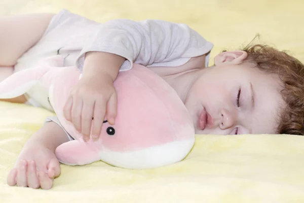 Menina menino dormindo abraçando uma baleia rosa de brinquedo. Pequena criança caucasiana dorme com um brinquedo suave — Fotografia de Stock