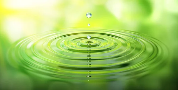 Springender Wassertropfen mit gruener Spiegelung und Wellen
