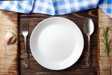 Pişirme arka plan konsepti. Vintage kesme tahtası, mavi damalı peçete, tabak ve çatal bıçak takımı. Üstte görüntü.