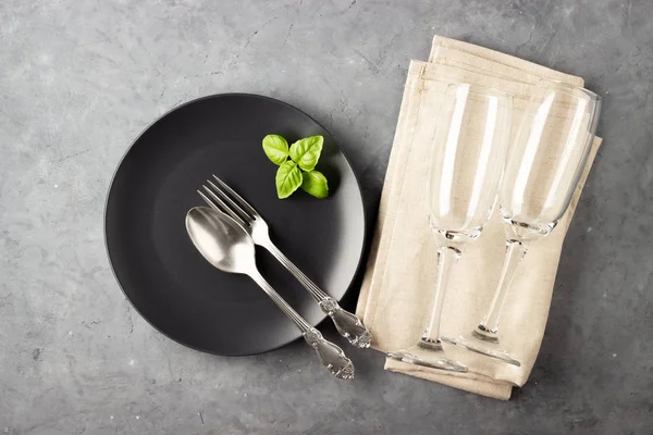 Table setting with black matte plate, wine glass and cutlery. View from above over gray concrete background.