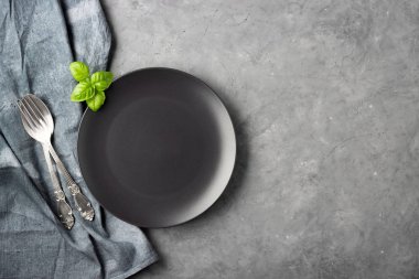 Masa ayarı. Gri beton arka plan üzerinde siyah plaka, çatal bıçak takımı ve peçete.