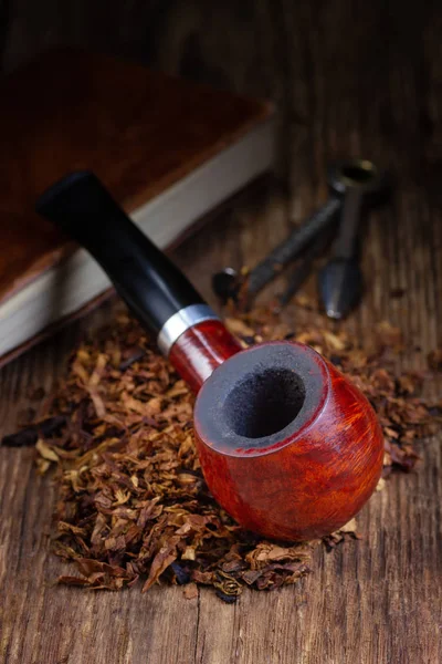 Smoking pipe and tobacco pile on vintage wooden table.