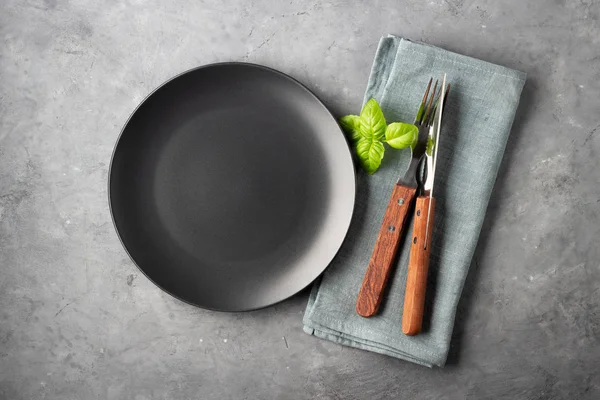 Masa ayarı. Gri beton arka plan üzerinde siyah plaka, çatal bıçak takımı ve peçete.
