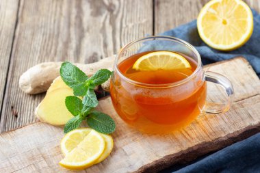 Ahşap rustik masada limon, nane ve zencefil ile bir bardak çay.