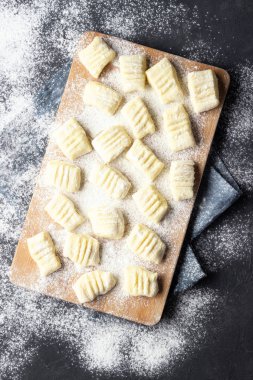 Kesme tahtası üzerinde un ile çiğ pişmemiş ev yapımı patates gnocchi. Üst te. Koyu arka plan.