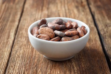 Ahşap bir masada beyaz bir kapta çiğ kakao çekirdekleri.