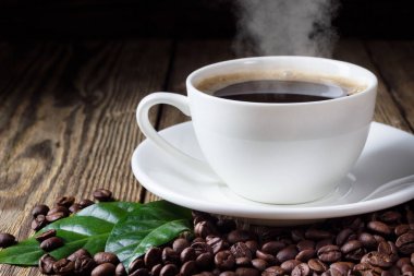 Ahşap bachground üzerinde kahve çekirdekleri ve yaprak ile sıcak kahve Fincan