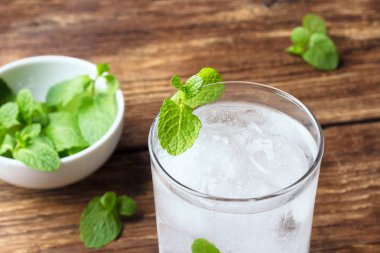 Ahşap arka planda buz ve nane ile su bardağı.