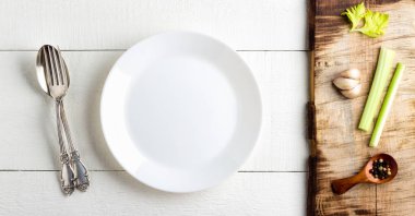 Yemek planı kavramı. Ahşap arka planda boş beyaz plaka, baharat ve çatal bıçak takımı.