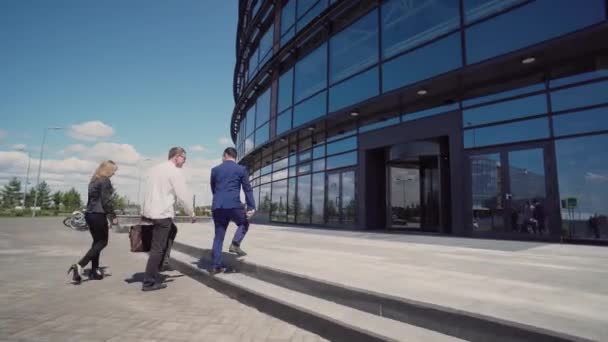 Три бізнесмени в ділових костюмах в сонячну погоду швидко входять в офіс — стокове відео