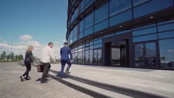 Drei Geschäftsleute in Business-Anzügen bei sonnigem Wetter betreten schnell das Büro — Stockvideo