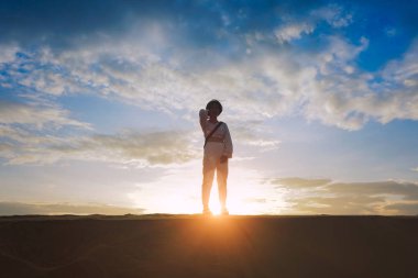 gün batımında kum ulanında duran kadının arkadan aydınlatmalı görünümü