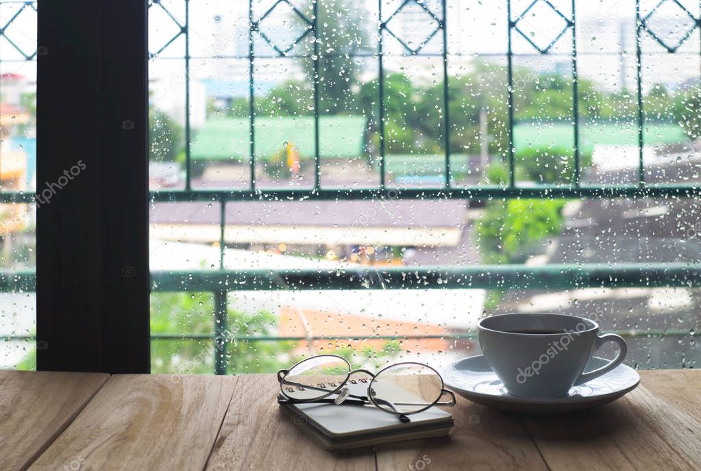 White cup of coffee with glasses by wet window