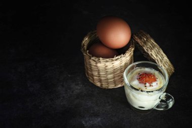 Küçük cam bardakta haşlanmış yumurta ve hasır sepette taze yumurta 