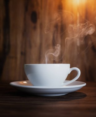 Kahveli beyaz fincan ve ahşap masada buhar.