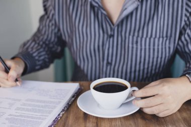 kağıtlar ve kahve ile masada oturan çizgili gömlek adam kırpılmış atış