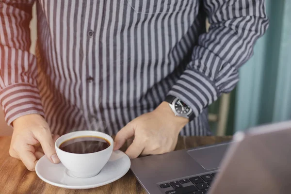 cropped shot of man standing by table with hot coffee and laptop